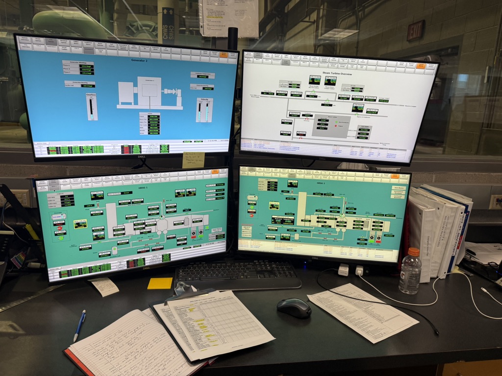 Poste de supervision à quatre écrans affichant les synoptiques colorés d'une production d'eau glacée, sur un bureau avec clavier et documents