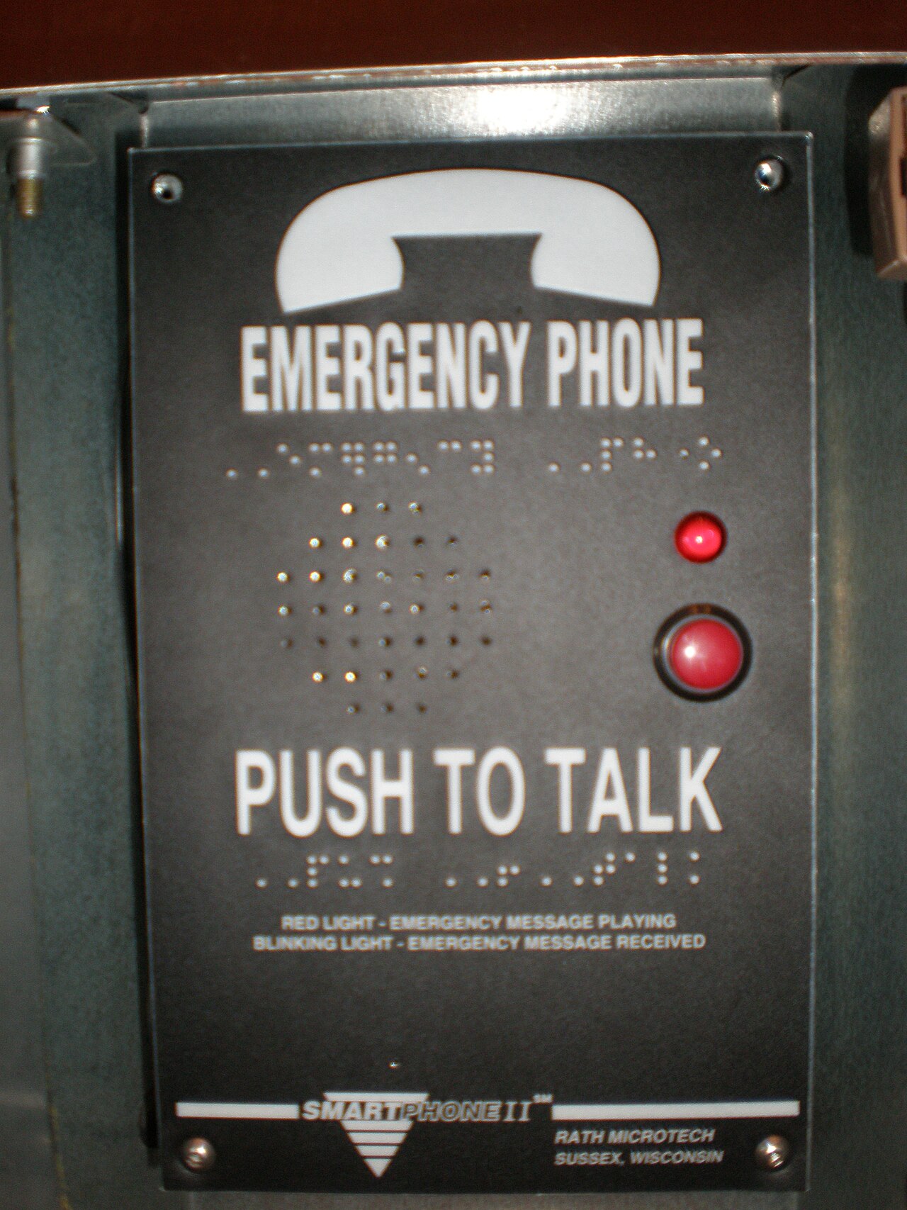 Téléphone d'urgence dans une cabine d'ascenseur : haut-parleur, bouton d'appel rouge et mention Push to talk